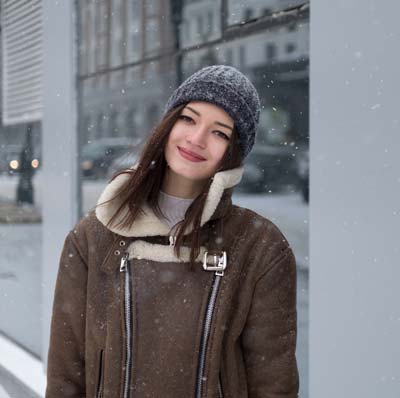 A photo of a smiling woman wearing a brown jacket and a gray beanie